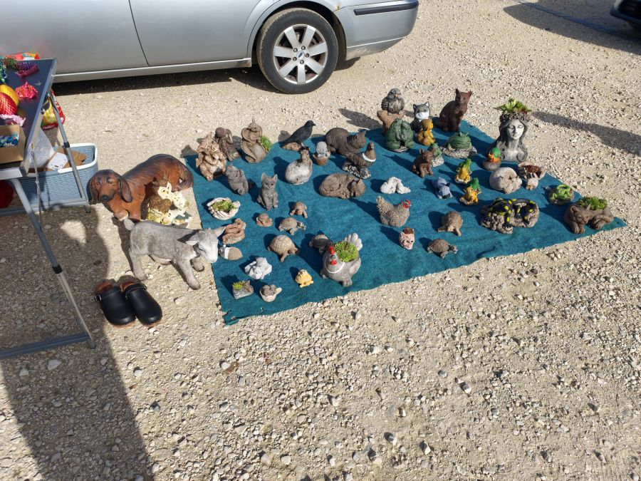 Deko-Gartenfiguren aus Stein bzw. Keramik in Tierform auf einer Picknickdecke ausgelegt, dahinter größere Figuren wie Hund, Eule und Esel.