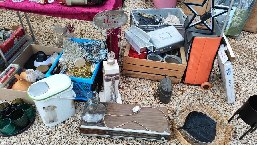 Haushaltswaren und Deko auf Kiesboden: ein altes SABA-Röhrenradio, eine Feldflasche, eine Geldkassette und Weihnachtsdeko.