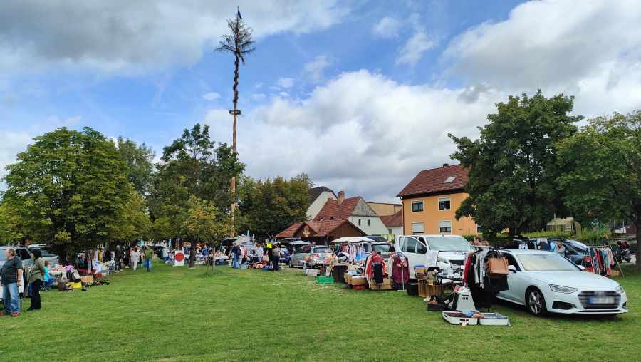 Weite Wiese mit Maibaum und Flohmarktständen in Amberg-Raigering, im Vordergrund ein weißer Audi und ein Kleiderständer.