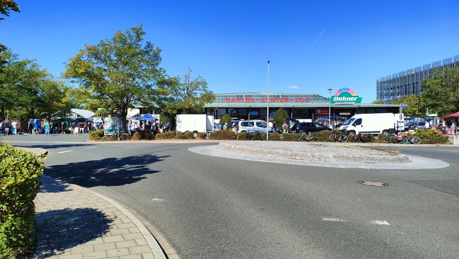 Übersicht eines Flohmarkts auf dem Parkplatz eines Dehner-Gartencenters in Erlangen, mit Marktständen entlang der Hecke und einem Kreisverkehr im Vordergrund.