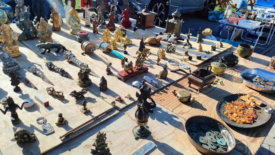 Auslage mit tibetischen Gebetsmühlen, Ritualdolchen, Bronzefiguren, chinesischen Münzen und rohem Bernstein auf einem Flohmarkt-Sammlerstand.