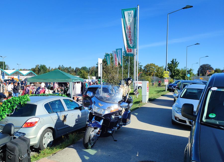 Flohmarkt am Hagebaumarkt Feucht: Verkaufspavillon mit Kleiderständern, davor eine blaue Honda Gold Wing mit Deko-Skelett und eine Royal Enfield, dahinter hagebau-Fahnen.