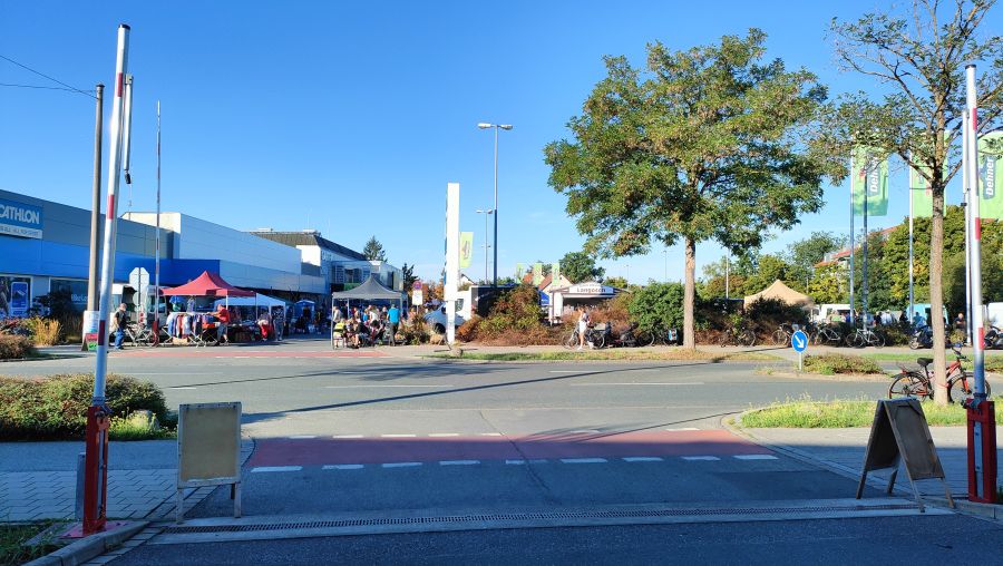 Flohmarkt auf einem Parkplatz neben einem Decathlon-Markt in Fürth, von der Straße aus gesehen: Pavillonzelte mit Kleiderständern, ein Langos-Imbisswagen und eine Reihe gebrauchter Fahrräder; im Vordergrund eine Straße mit rotem Radweg.