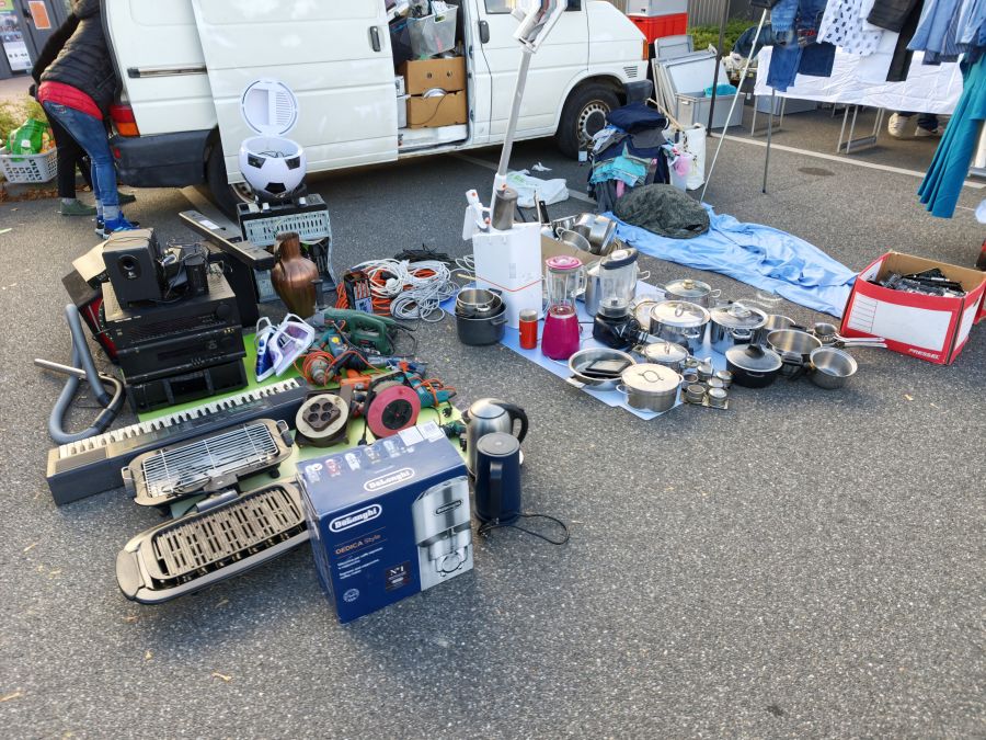 Haushaltsgeraete, Kochgeschirr und Werkzeug als Flohmarkt-Angebot vor einem Transporter