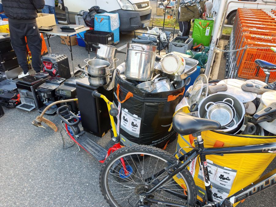 Kochtoepfe, Kaffeemaschinen und ein Fahrrad als Flohmarkt-Angebot vor einem Transporter