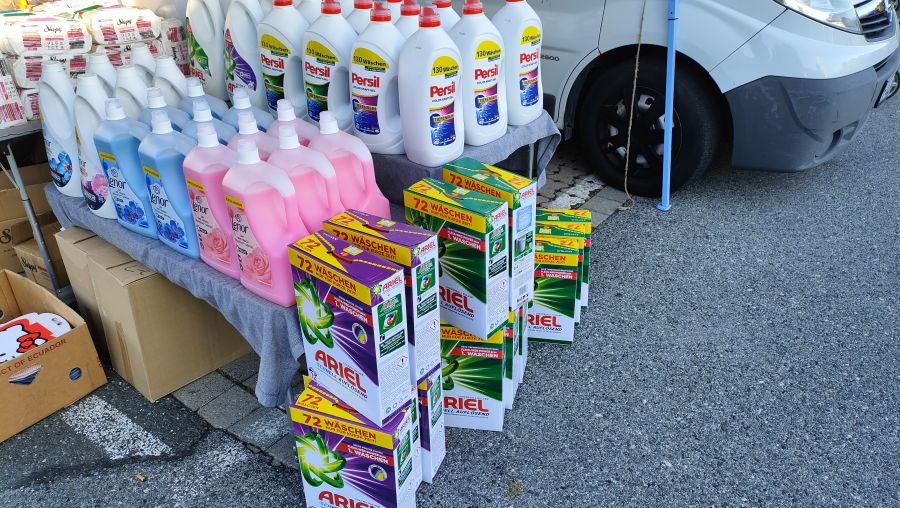 Verkaufsstand mit Waschmittel- und Weichspüler-Großflaschen (Persil, Lenor), Ariel-Waschpulver-Kartons und Windelpaketen auf dem Flohmarkt am OBI-Parkplatz Fürth.