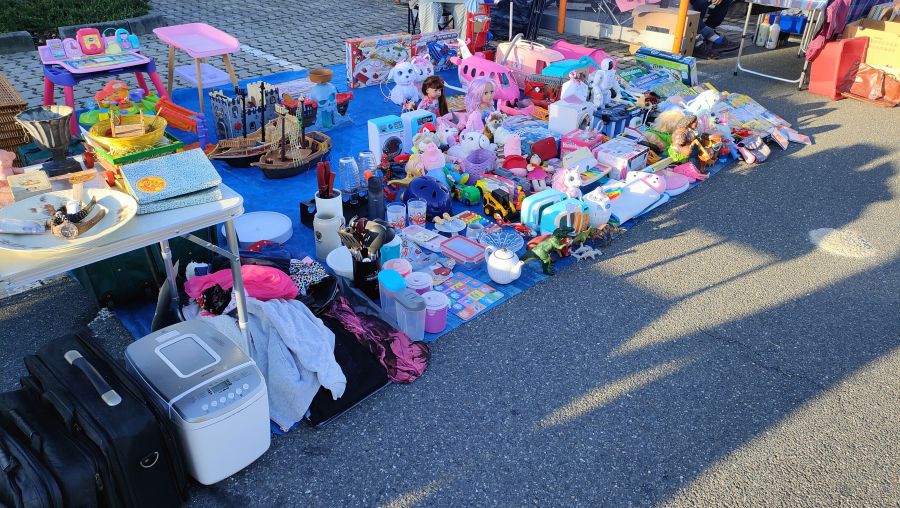 Ausgebreitete Flohmarkt-Bodenauslage mit vielen Spielsachen – Puppen, Plüschtieren, Spielküche, Ritterburg, Piratenschiff – sowie Haushaltswaren, Armbanduhren und einem Brotbackautomaten auf dem OBI-Parkplatz Fürth.