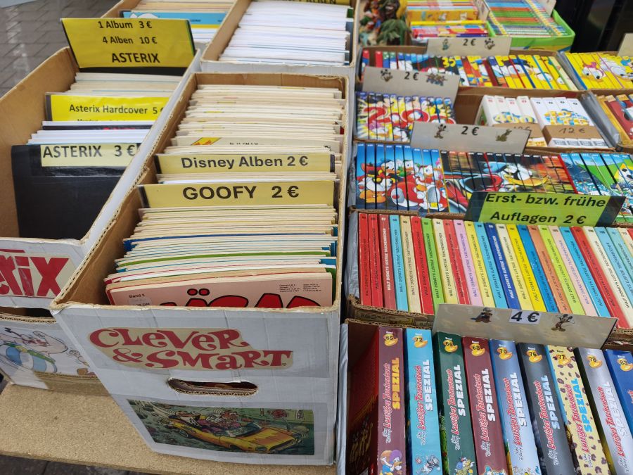 Mit Preisschildern sortierte Kartons voller Comic-Hefte auf dem Flohmarkt: Asterix, Clever & Smart, Disney-Alben und Lustiges Taschenbuch.