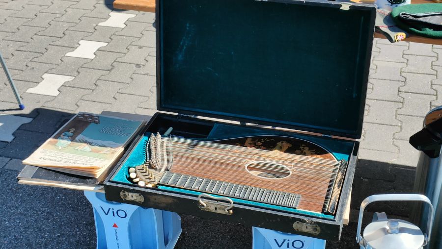 Alte Konzertzither in ihrem geöffneten Holzkoffer, daneben ein Zither-Notenbuch, auf einem Flohmarkt.