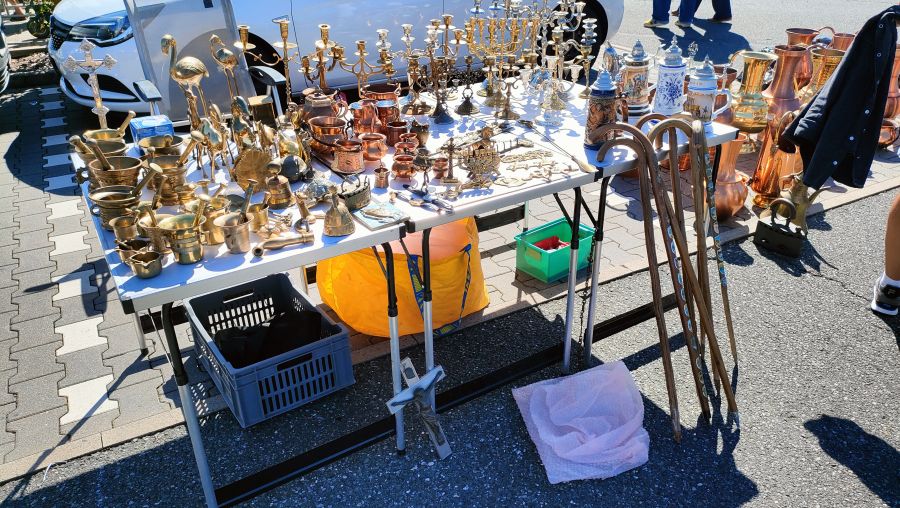 Ein Tisch dicht gestellt mit Messing-Mörsern, vielen Kerzenleuchtern, Kupferbechern und Bierkrügen auf einem Flohmarkt.