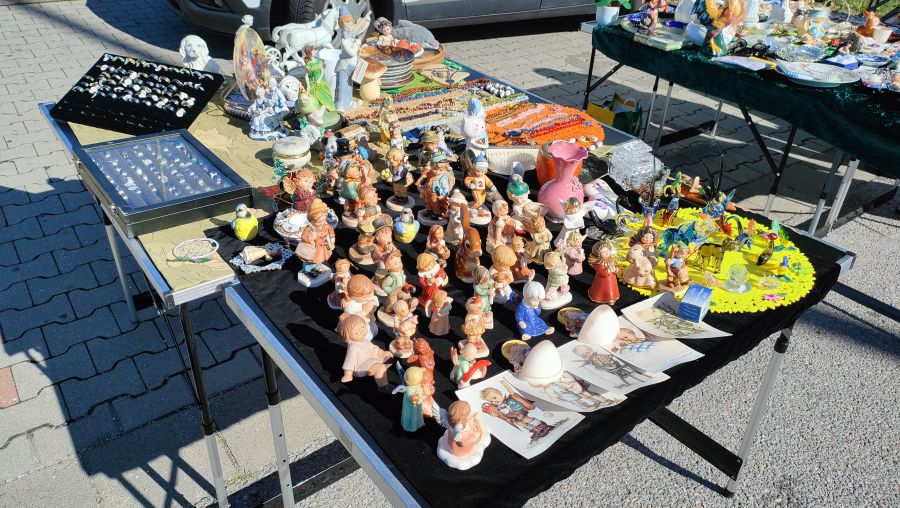 Voll gestellter Tisch mit vielen Porzellan-Sammelfiguren im Hummel-Stil, Engelfiguren, Glastieren und einem Setzkasten mit Ringen auf einem Flohmarkt.