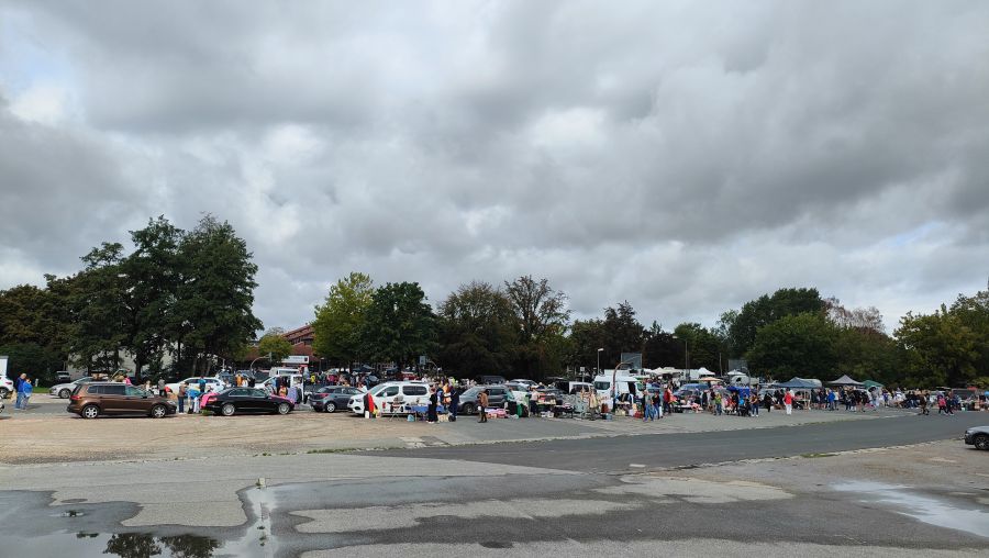 Breite Weitwinkelaufnahme des Flohmarkts Neumarkt i.d.Opf. vor der Jurahalle mit langer Standreihe, parkenden Autos und Besuchern.