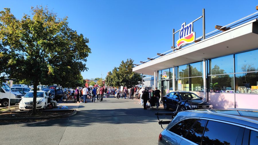 Flohmarkt entlang der Zufahrt eines Nürnberger Einkaufszentrums mit dm-Markt, Ständen, Kleiderständern und vielen Besuchern.
