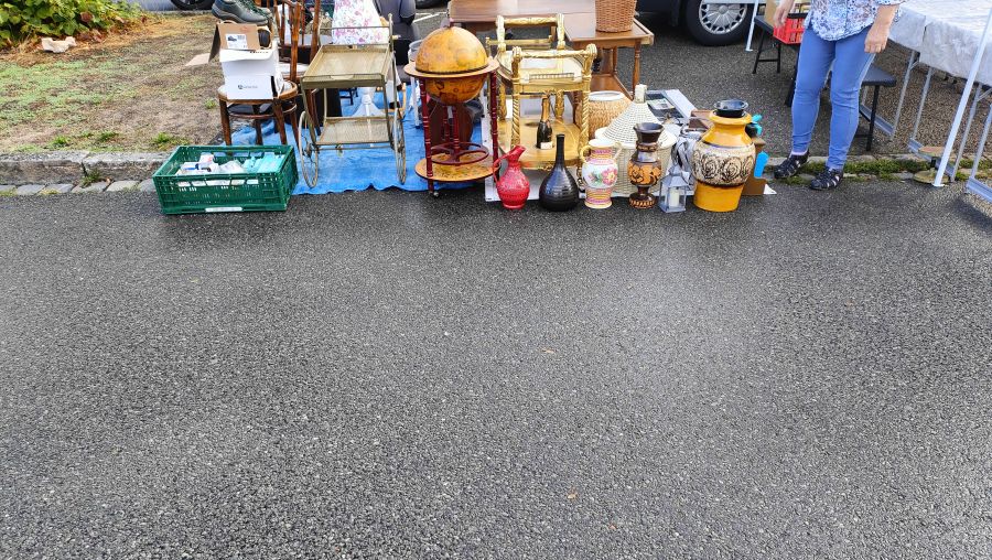Deko- und Antikstand mit einer hölzernen Globus-Bar, einem goldfarbenen Servierwagen, mehreren Vasen und Krügen sowie einer großen gelb-braunen Bodenvase auf dem Flohmarkt.