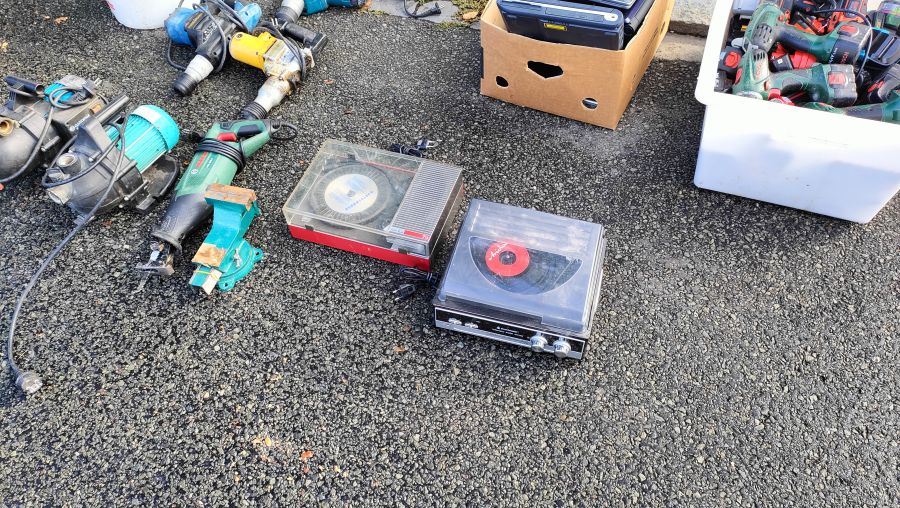 Zwei kleine tragbare Kofferplattenspieler auf dem Boden, umgeben von gebrauchten Elektrowerkzeugen wie einer Bosch-Säbelsäge und mehreren Akkuschraubern.