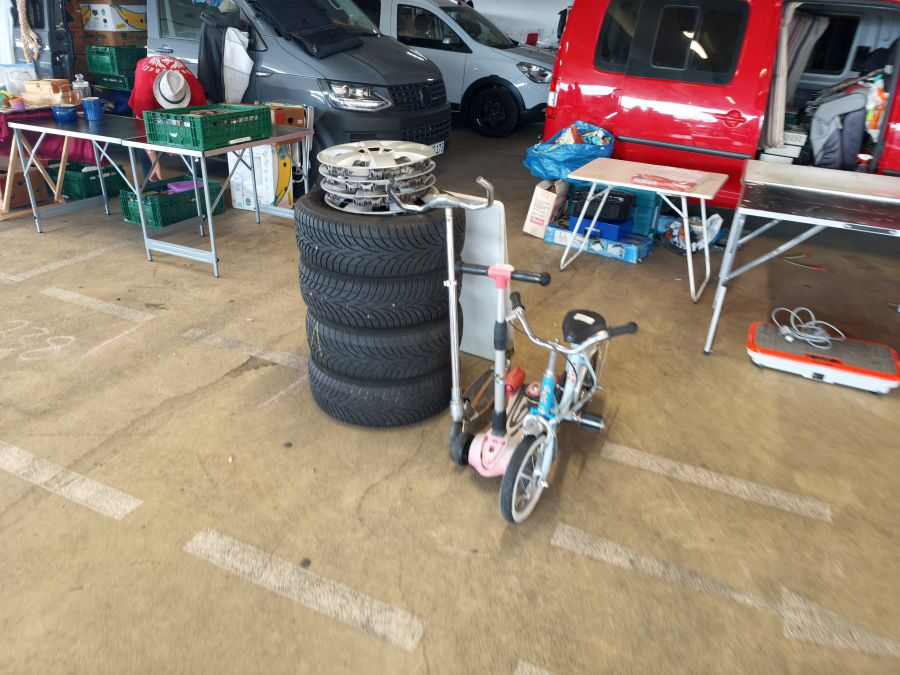 Stapel aus vier Alufelgen mit Reifen neben einem Kinder-Tretroller auf einem Flohmarkt.